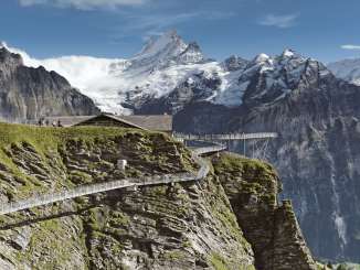 Der First Cliff Walk im Sommer, mit Besuchern auf dem Steg, dahinter grüne Hänge, hohe Berge und ein klarer blauer Himmel.