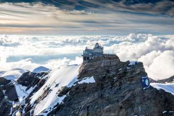 Blick von oben auf das Jungfraujoch, umgeben von Schnee, im Hintergrund ein Nebelmeer.