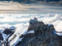 Blick von oben auf das Jungfraujoch, umgeben von Schnee, im Hintergrund ein Nebelmeer.