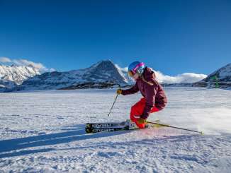 Skifahren im Skigebiet Grindelwald - Wengen. Skifahrer ziehen in schönen Schwüngen ihre Spuren durch den Schnee. Im Hintergrund blickt man auf das Dreigestirn Eiger, Mönch und Jungfrau.