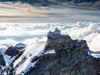 Blick von oben auf das Jungfraujoch, umgeben von Schnee, im Hintergrund ein Nebelmeer.