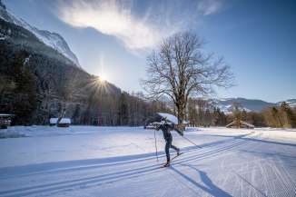 Eine Frau fährt Langlaufski in Grindelwald. Sie ist in Bewegung im Gegenlicht, im Hintergrund ein kahler Baum und mehrere Holzhäuser.
