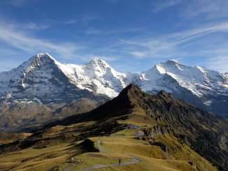 Aussicht auf den sommerlichen Männlichen mit dem verschneiten Dreigestirn Eiger, Mönch und Jungfrau im Hintergrund.