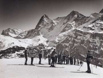 Winternostalgie in Mürren. Die Gruppe schaut dem Skilehrer gespannt zu. Im Hintergrund stehen die verschneiten Eiger und Mönch.