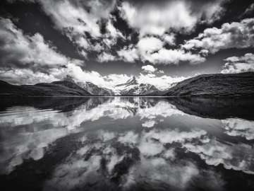Wolken spiegeln Sich im klaren Bachalpsee auf der First. Die Aufnahme ist in Graustufen.