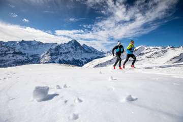 Zwei Läufer beim Winter Trail Running auf Grindelwald First, im Hintergrund der Eiger.