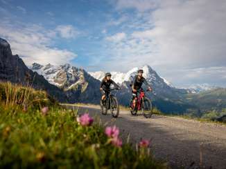  Zwei Biker fahren auf der grossen Scheidegg Richtung First. Im Hintergrund sieht man Grindelwald als Tal .